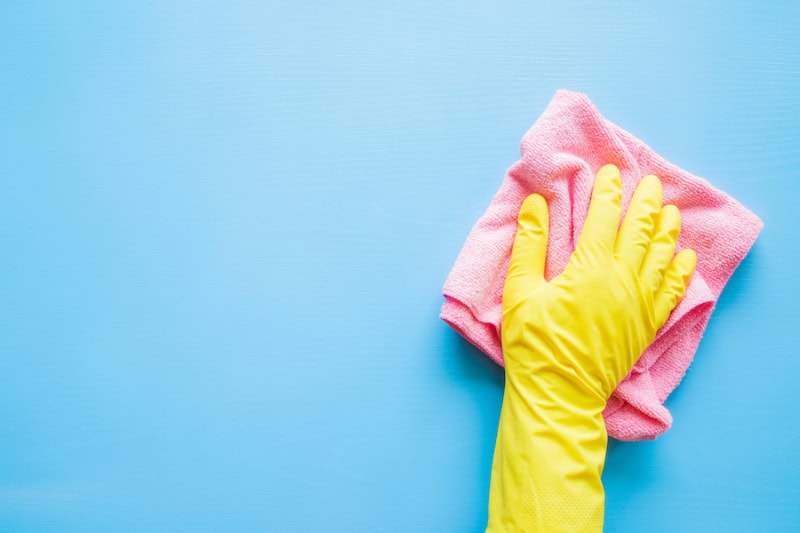 Does an AC Kill Mold? Hand in rubber protective glove with microfiber rag wiping blue table, wall or floor surface in room.