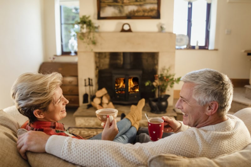 How to Keep Warm During Extreme Cold Weather. A couple sitting on the couch by a fire.
